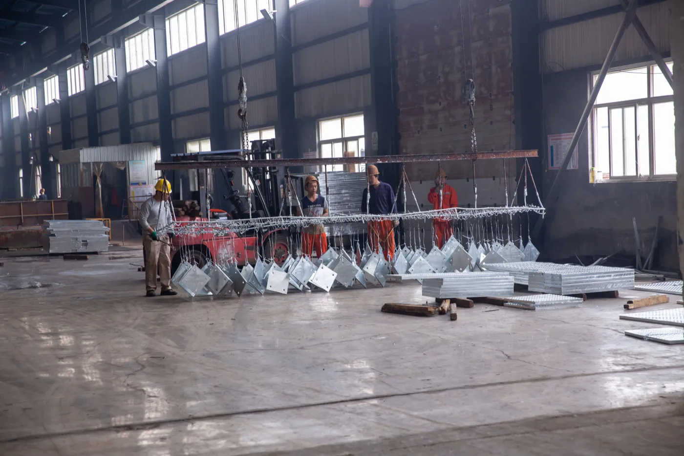 Workers preparing steel components on a lifting rack in the galvanizing workshop