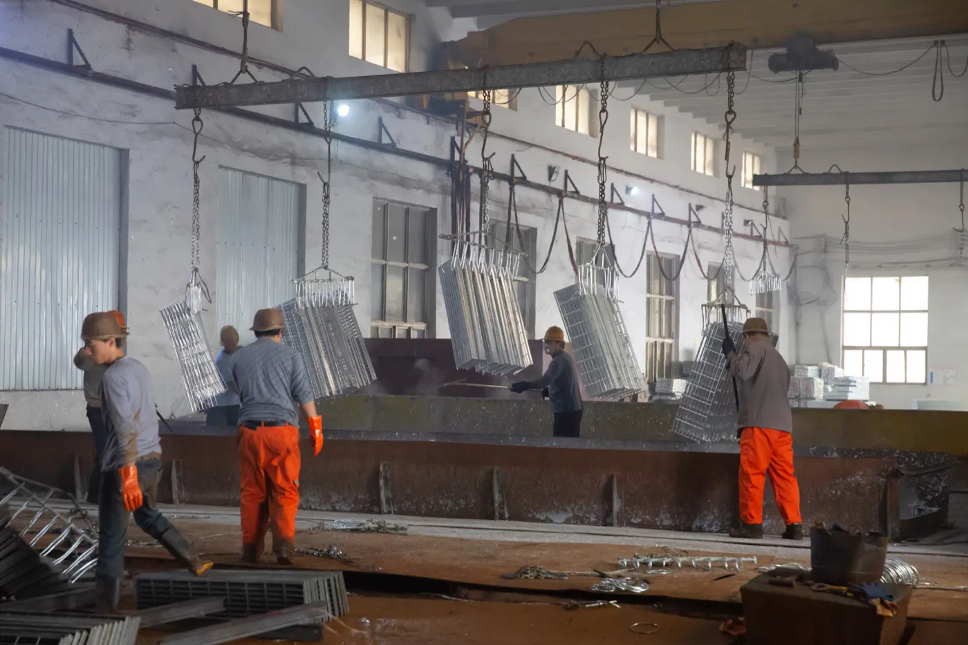 Workers handling steel grating panels at a hot-dip galvanizing bath