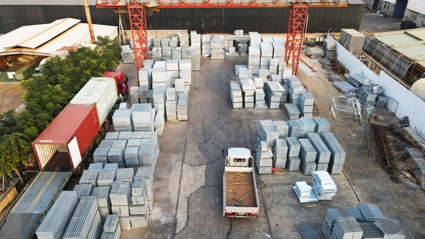 Factory dispatch yard with steel grating stock, trucks and shipping containers