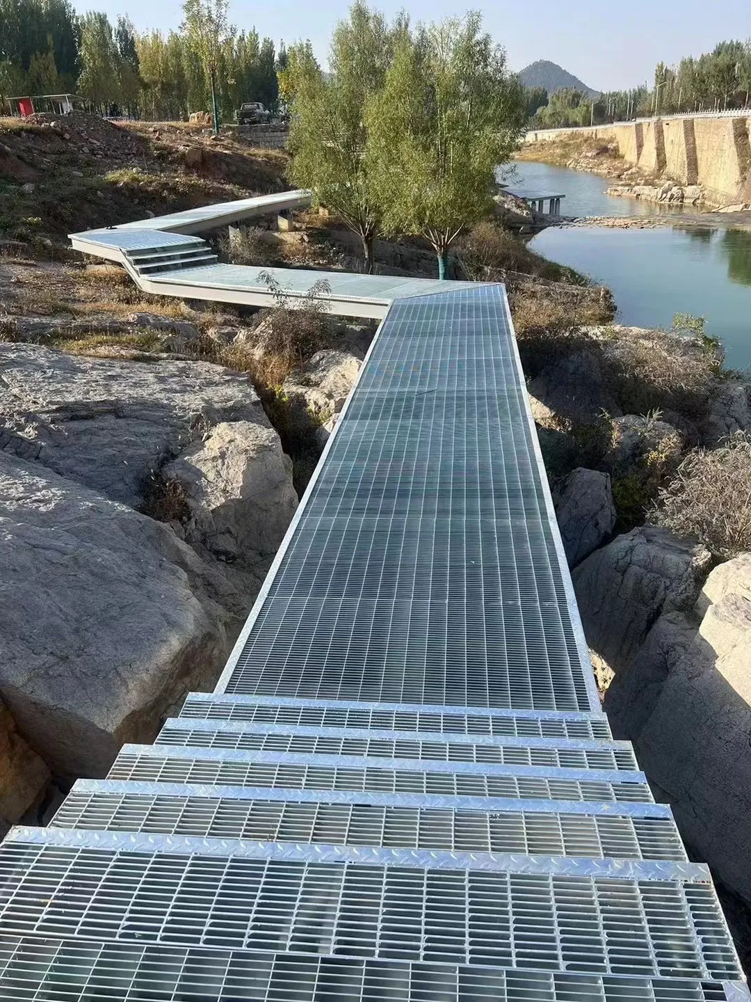 Steel grating boardwalk under construction beside a landscaped waterway