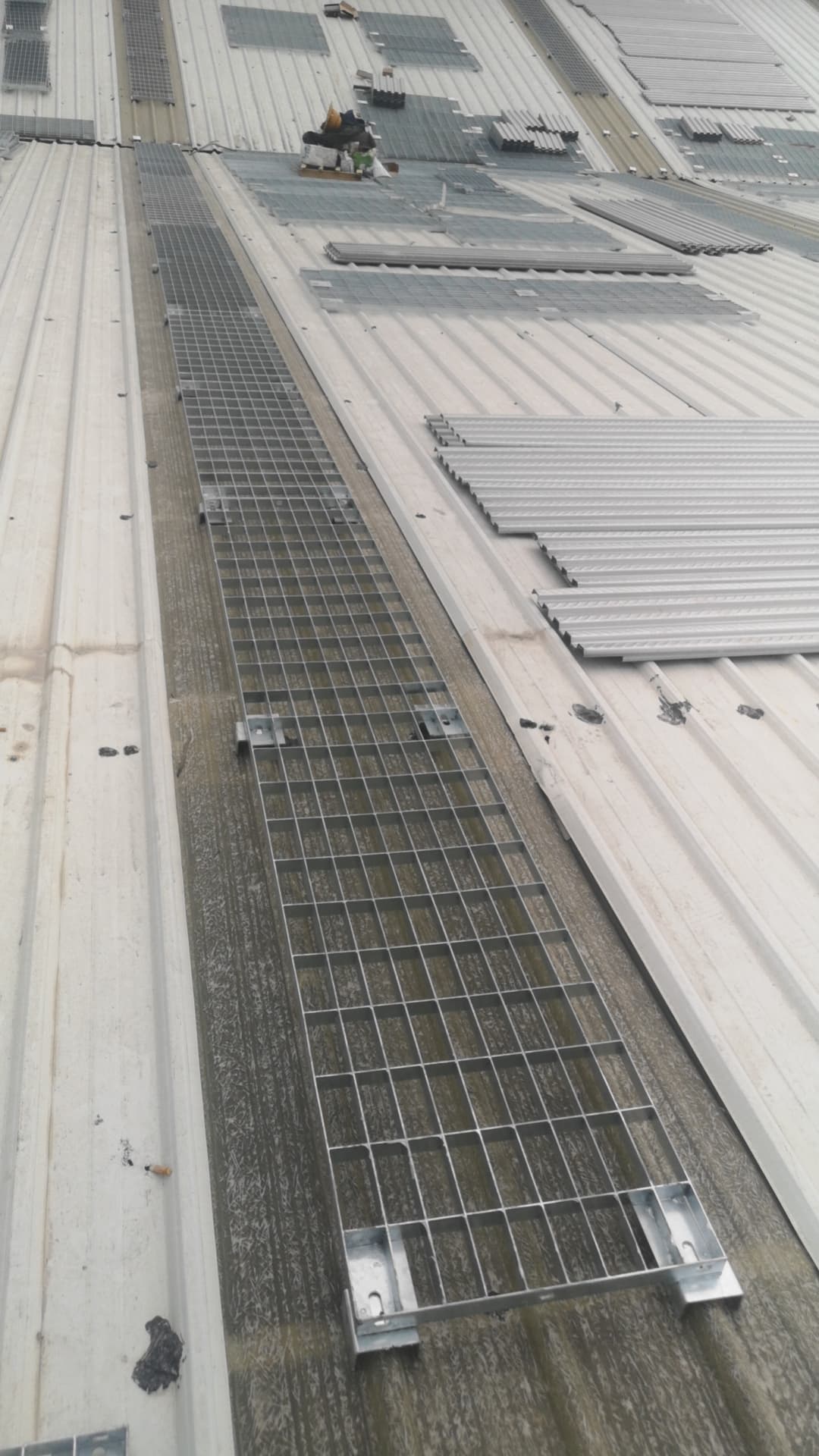 Narrow rooftop grating walkway aligned beside photovoltaic panel rows