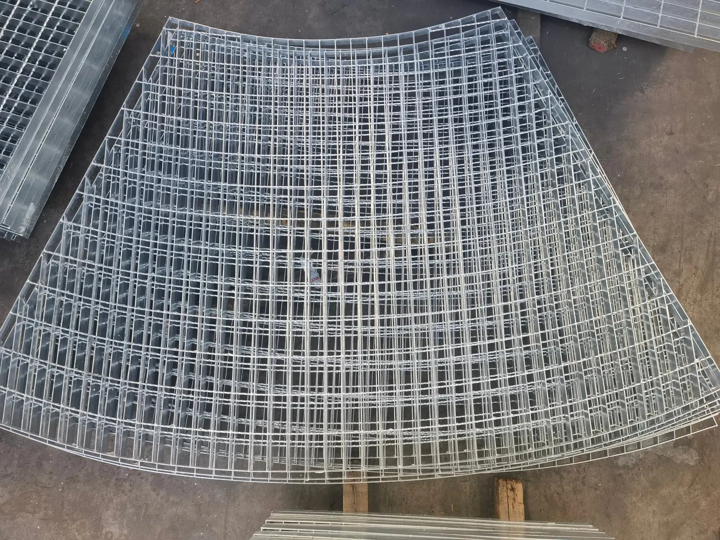 Stacked curved galvanized irregular steel grating panels on a workshop floor