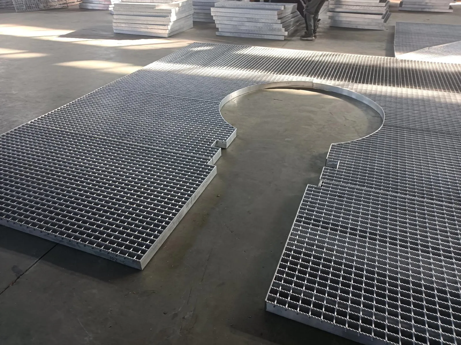 Galvanized irregular steel grating panels fabricated around a large circular opening on a workshop floor