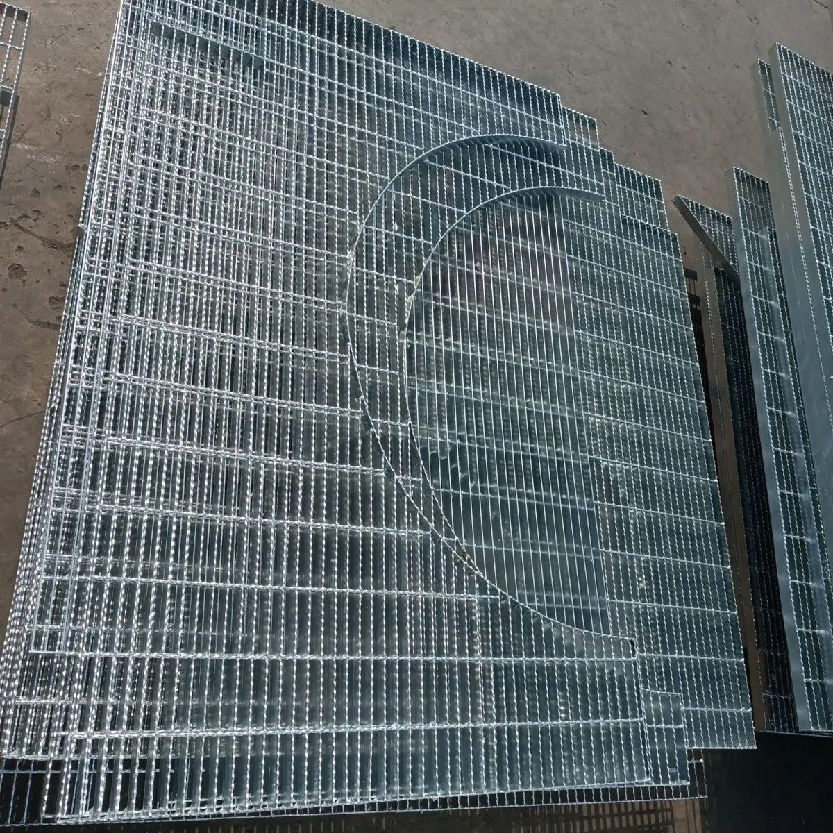 Stacked galvanized irregular steel grating panels with large circular cut-outs and stepped edges