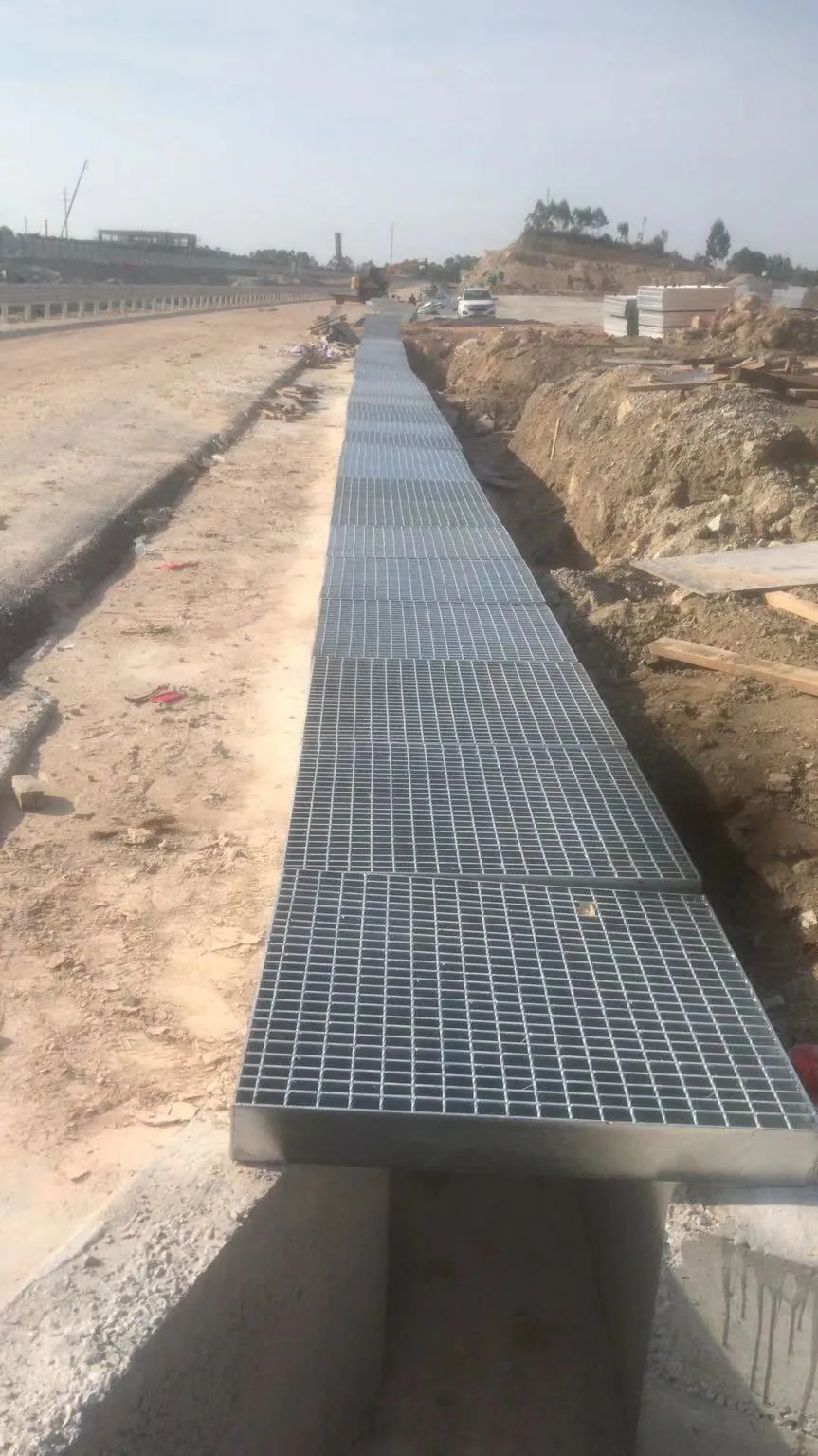 Long run of galvanized steel grating trench covers installed beside a roadway construction area