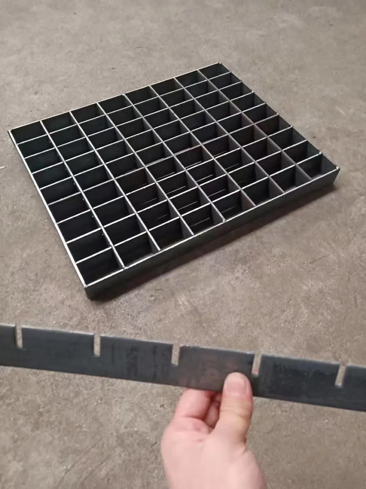 Worker holding a slotted bearing bar in front of an assembled press-locked grating panel
