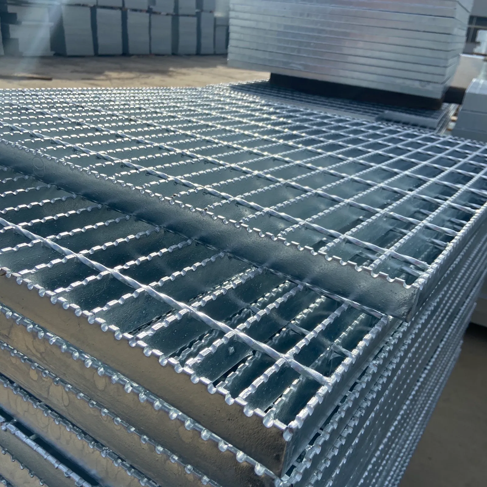 Close-up of stacked galvanized serrated grating panels showing toothed bearing bars