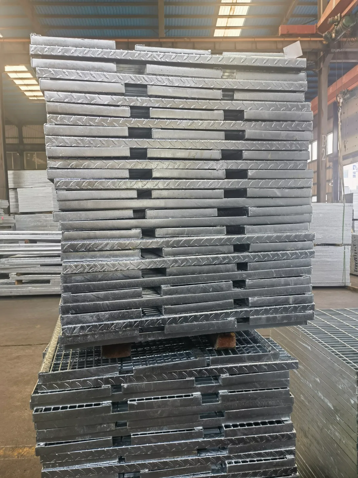 Galvanized stair tread grating panels stacked on timber supports in the workshop