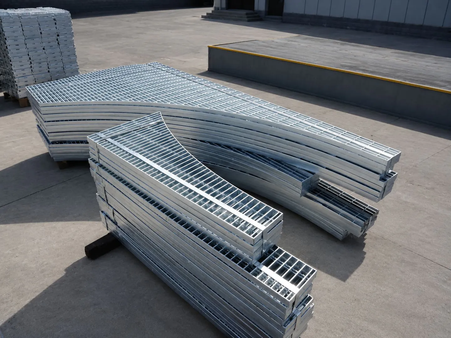 Curved and irregular galvanized grating panels stacked in a workshop yard