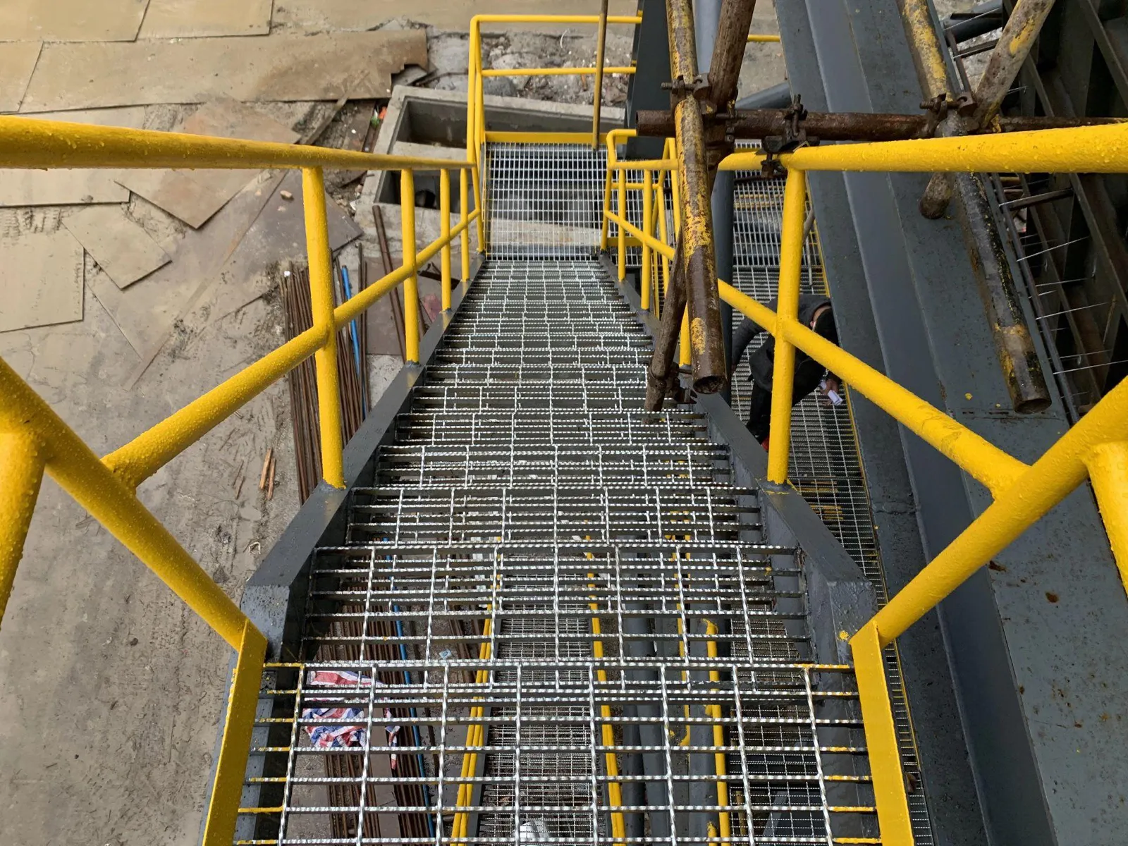 Installed steel grating stair treads with yellow safety railings on an industrial access stair