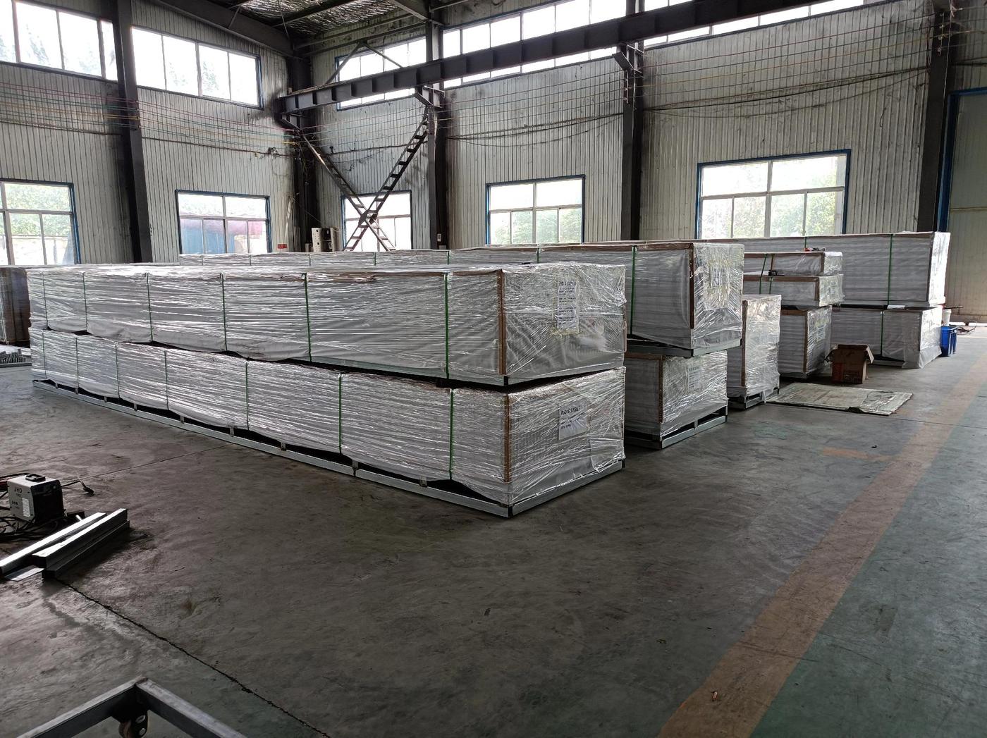 Wrapped bundles of aluminum grating panels stacked on supports inside a workshop