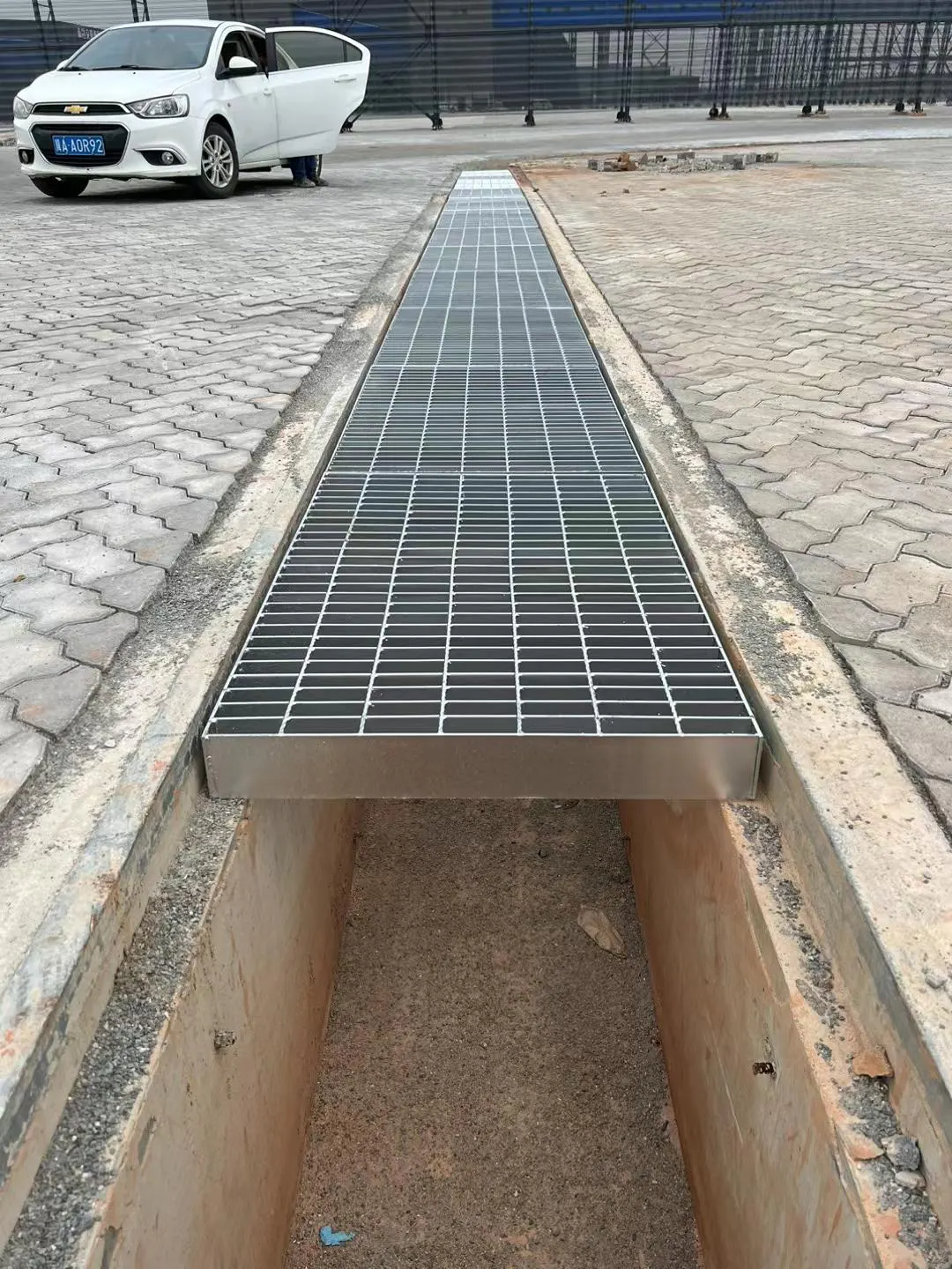 Galvanized trench cover grating installed across a paved industrial yard drainage channel