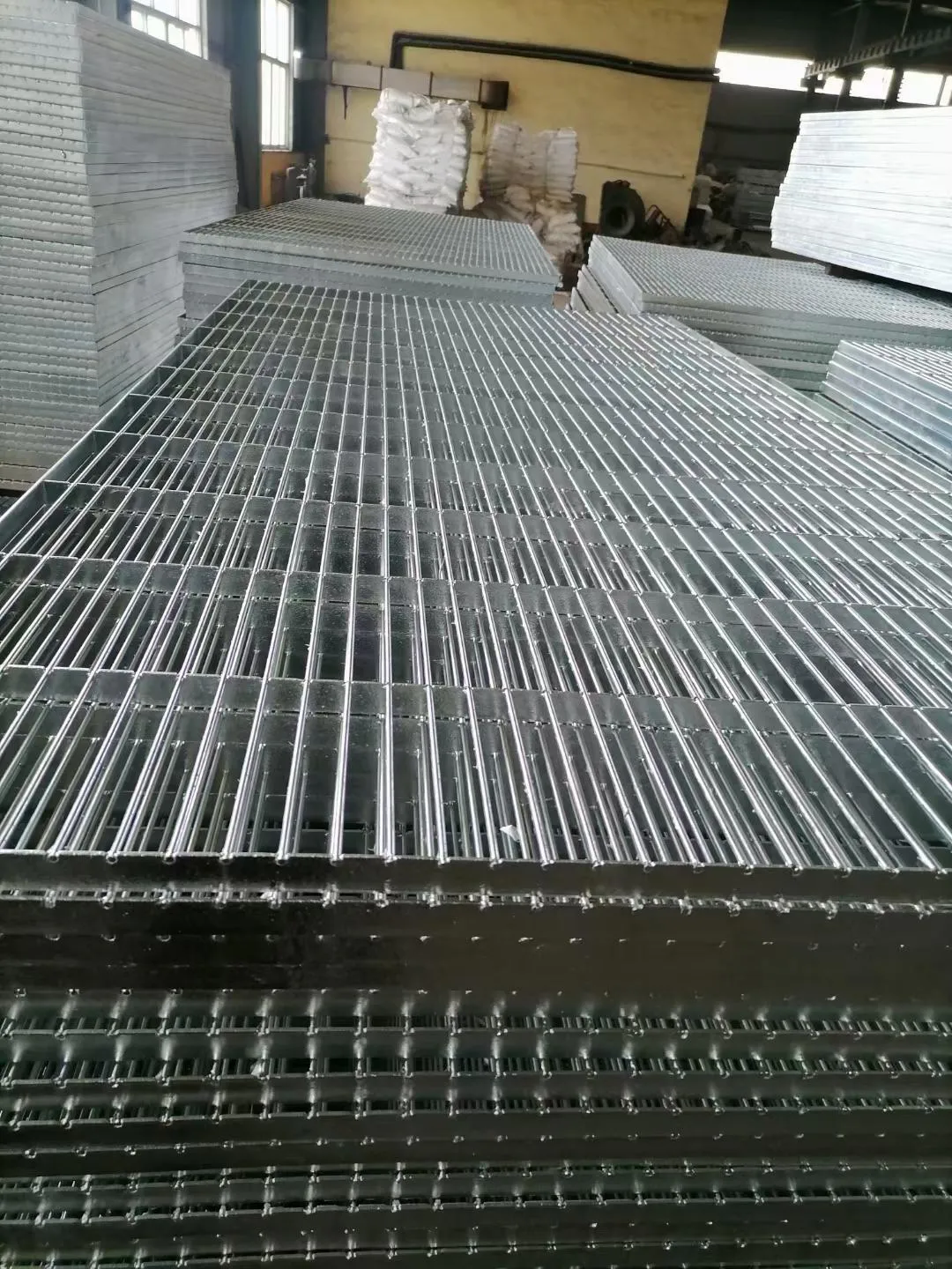 Stacked plain-surface hot-dip galvanized steel grating panels in the workshop