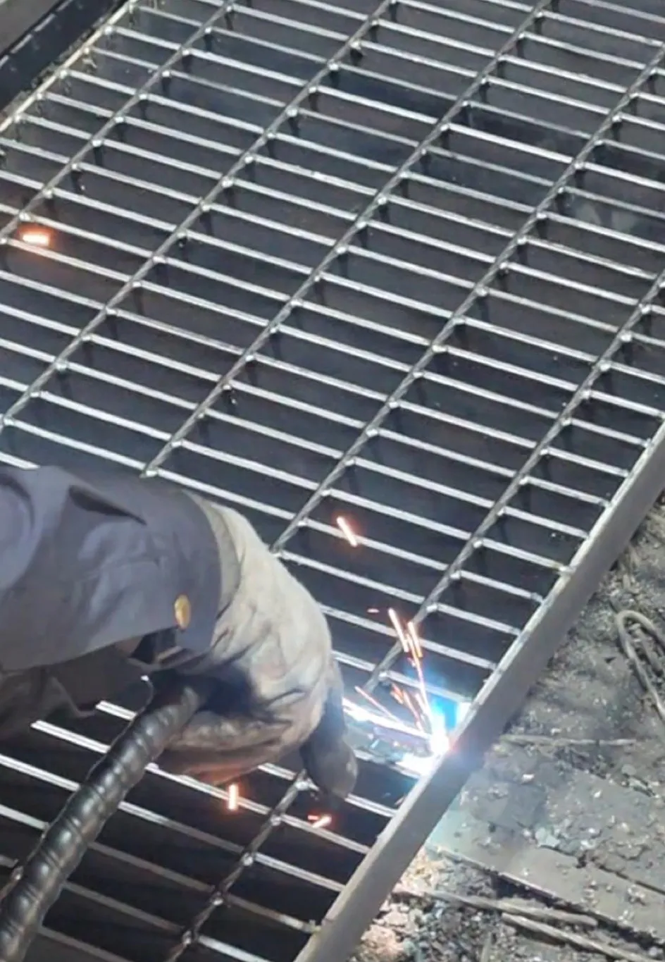 Worker manually welding the perimeter of a steel grating panel