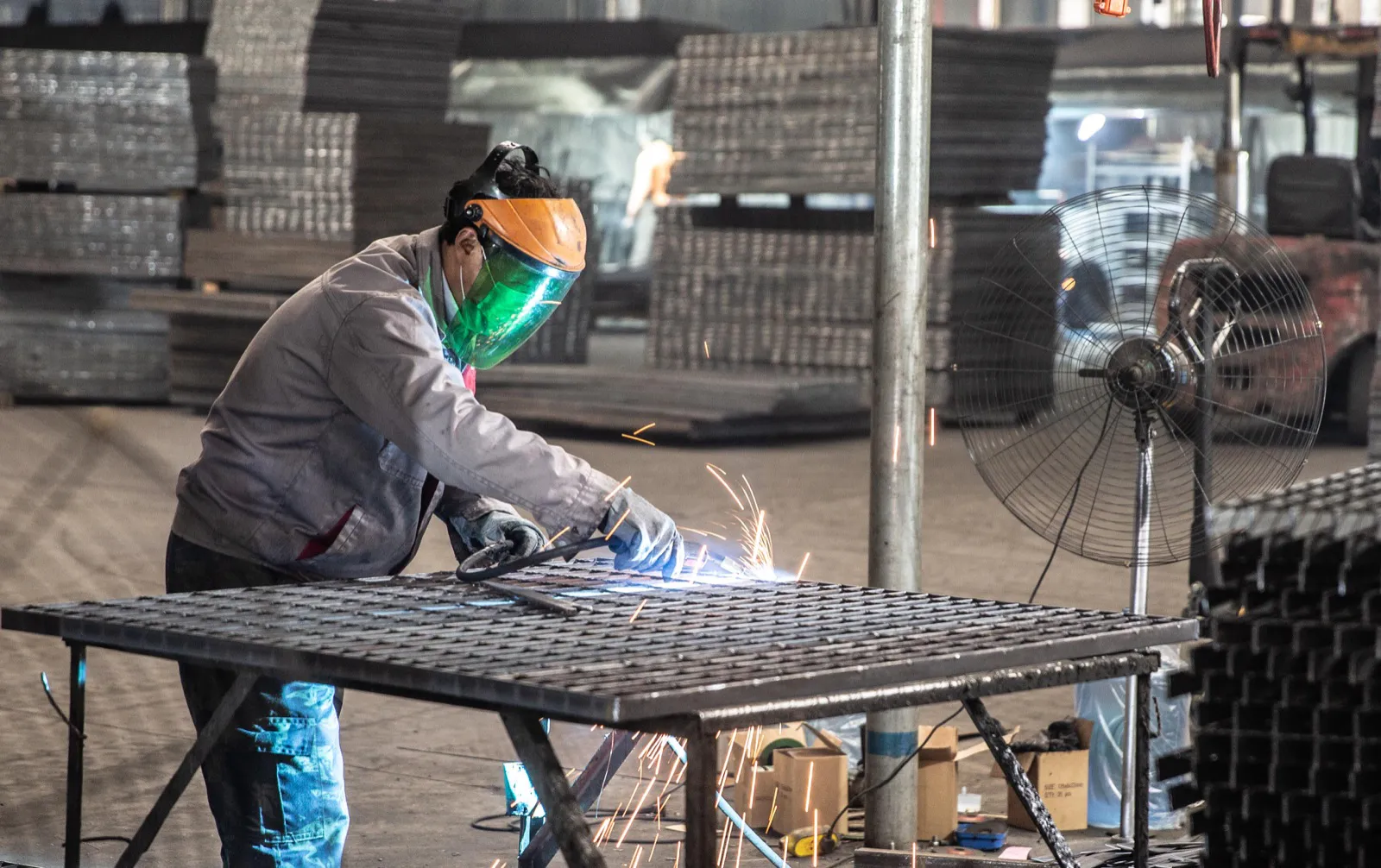 Welder manually fabricating a custom steel grating panel in the workshop