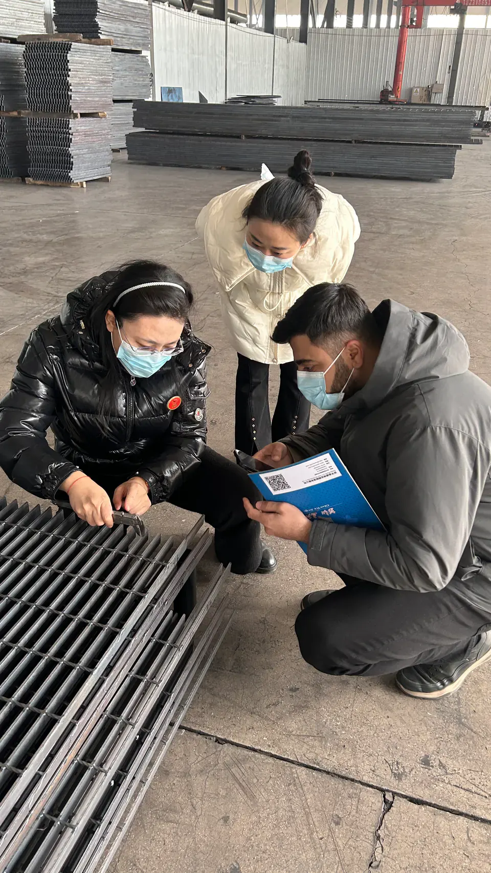 Three people examining welded steel grating together on the DONGFU factory floor