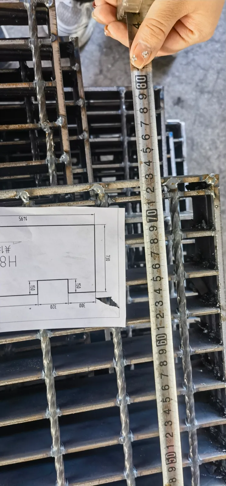 Custom steel grating panel checked against a fabrication drawing and measuring rule