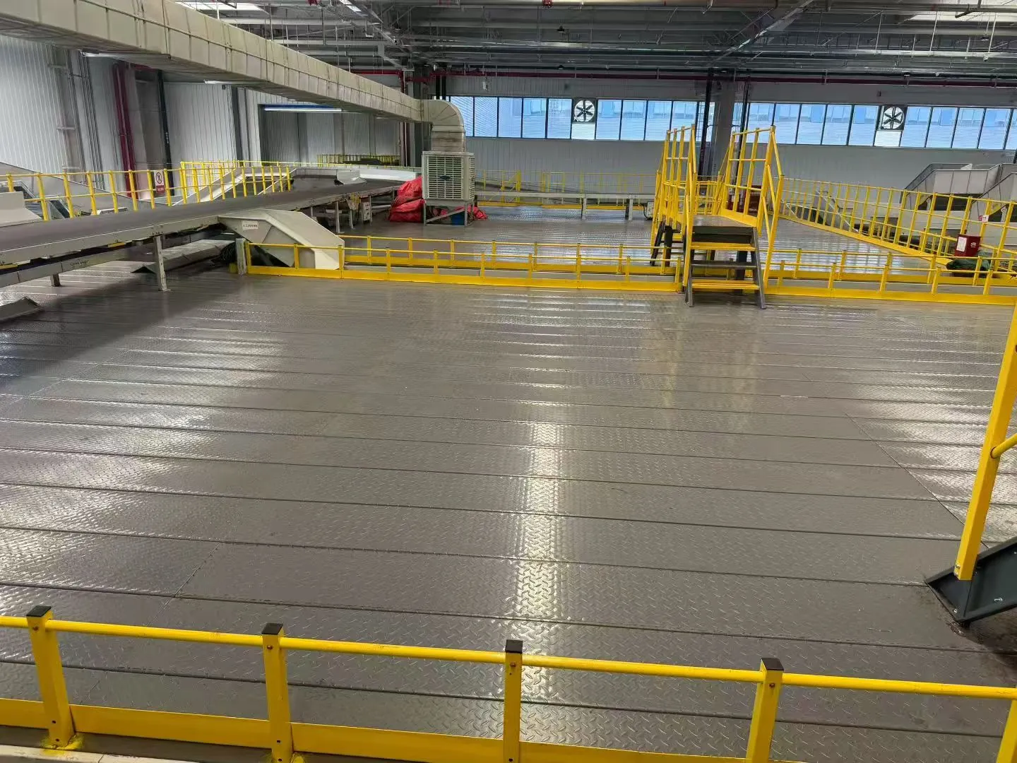 Checker-plate floor area with yellow guardrails and a stair crossing in the same logistics facility