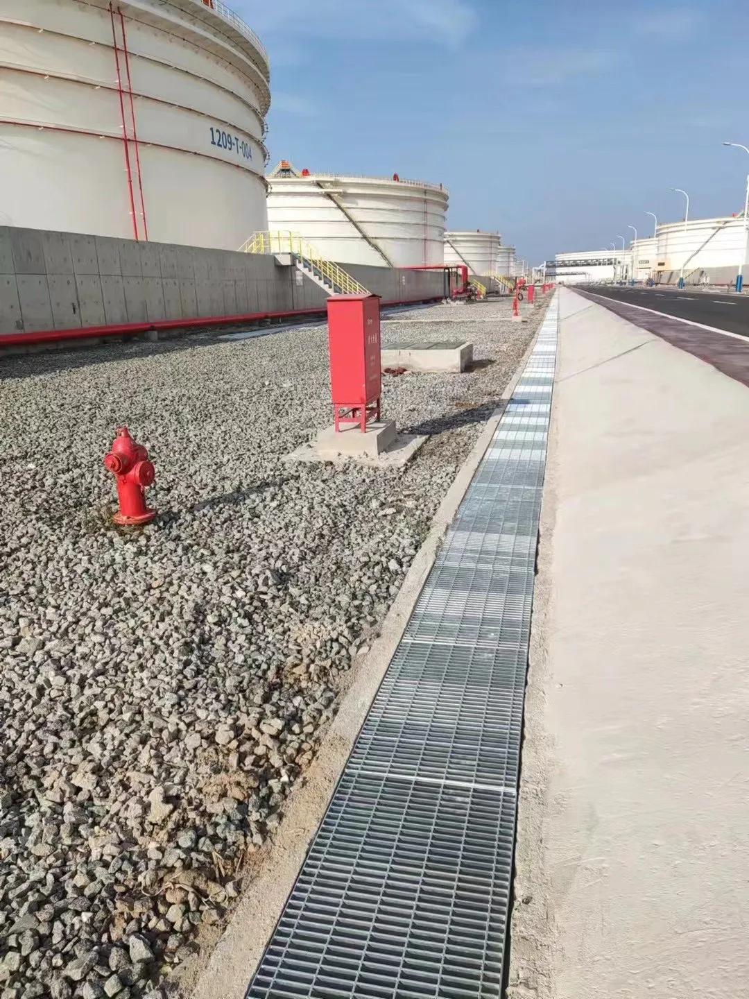 Steel grating drainage covers installed beside storage tanks in a petrochemical tank farm